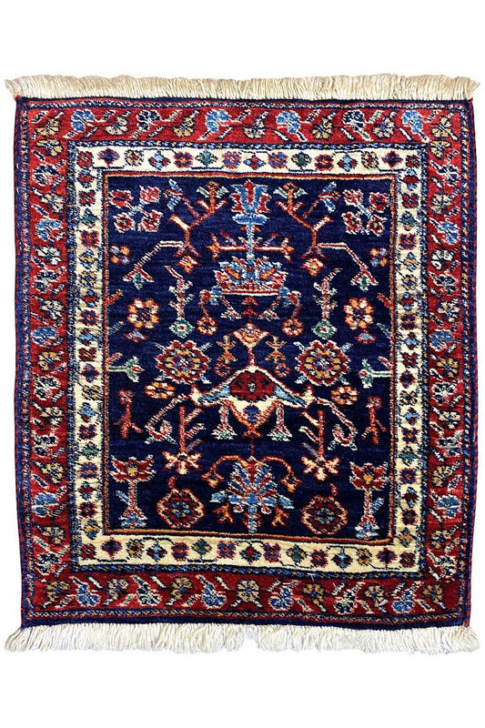 Square rug with a blue central medallion, red border ornaments, and fringes