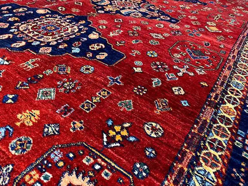 Detailed view of rug: red background with colorful small ornaments and a blue border