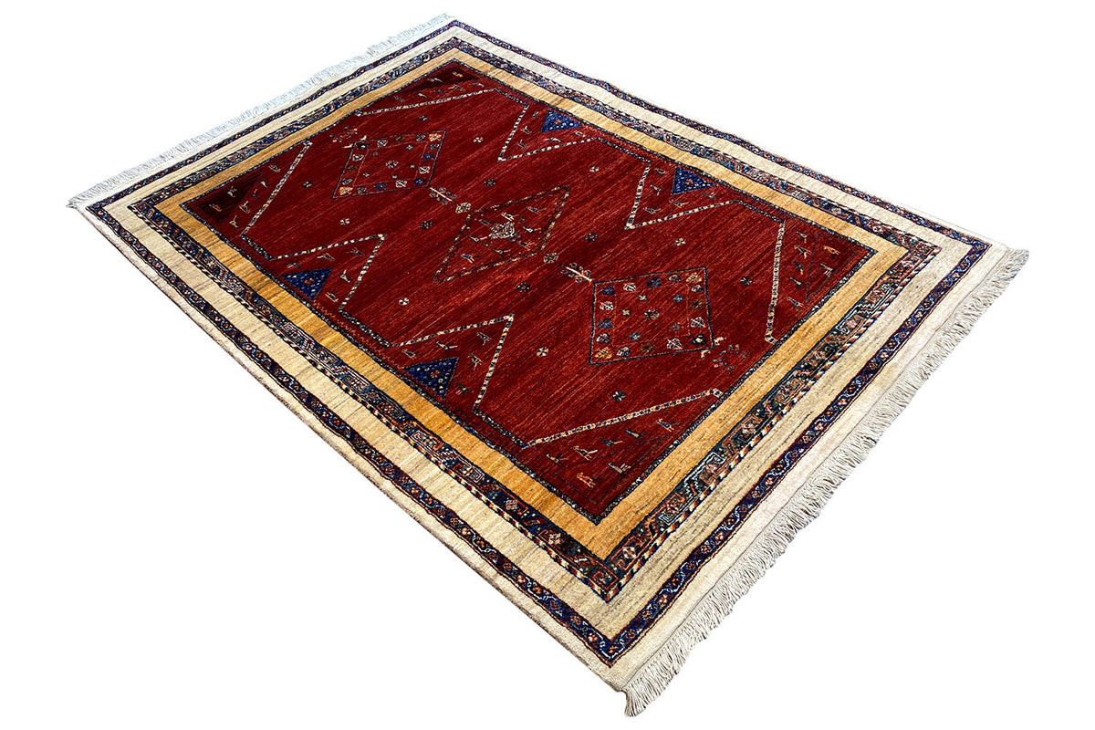 Oriental rug, red diamond field with a blue border, cream-colored bands, fringes along the edges