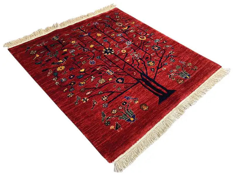 Red oriental rug with a tree motif, colorful ornaments and beige fringes, at an angle.