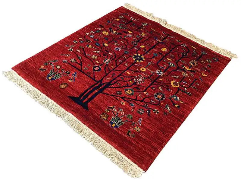Red oriental rug with a tree motif and colorful ornaments, beige fringe trim, angled.