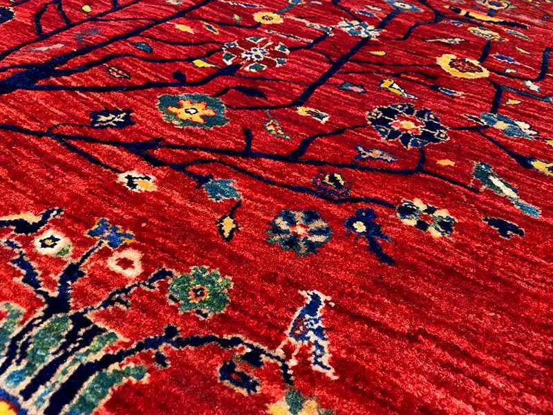Red Oriental rug with a detailed tree and floral pattern, close-up.
