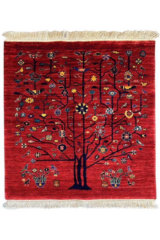 Red Oriental rug with a central tree, colorful ornaments, and beige fringes, viewed from the front.