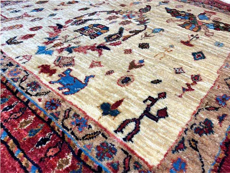 Close-up view of an oriental rug: beige pile with blue, red, and black motifs.