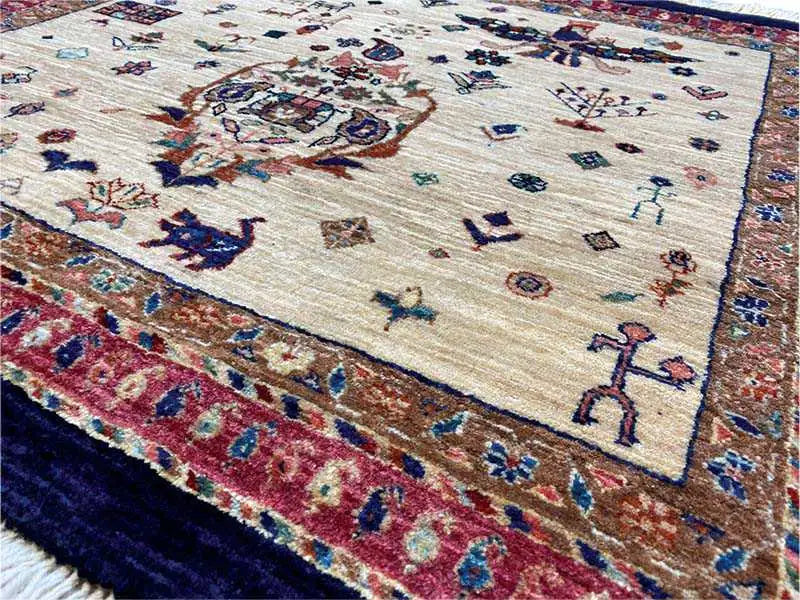 Close-up of a rug: beige background with blue and red figures, ornaments, and a colorful border.