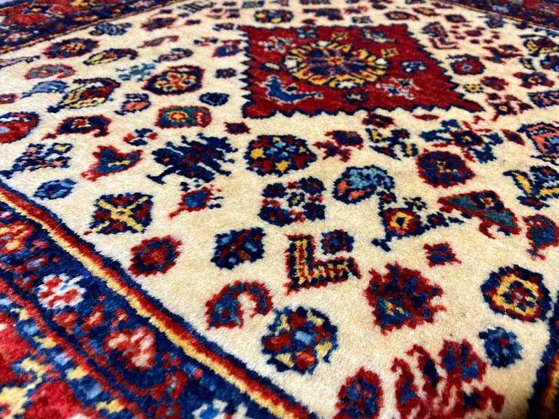 Close-up of an Oriental rug: cream-colored background with blue and red ornamentation and medallion