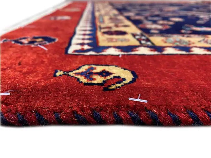 Close-up: red carpet pile with a multicolored pattern and fringes along the sides.