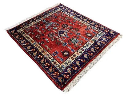 Red rug with a floral ornamental pattern, dark blue border, and fringes