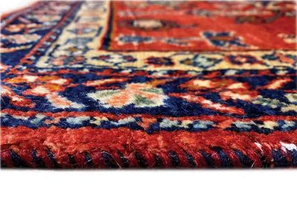 Close-up: red rug with blue-and-white patterns and a jagged fringed edge