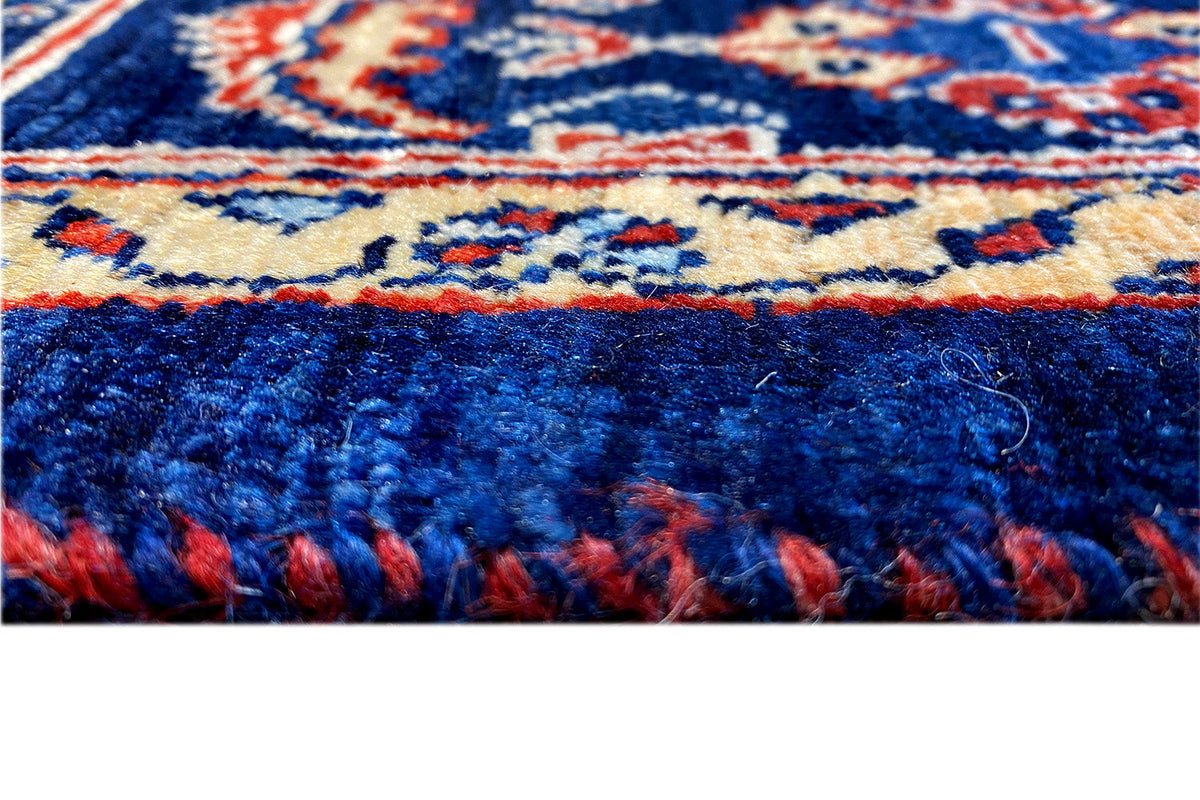 Oriental rug detail: blue border, multicolored pattern, and fringes along the bottom edge