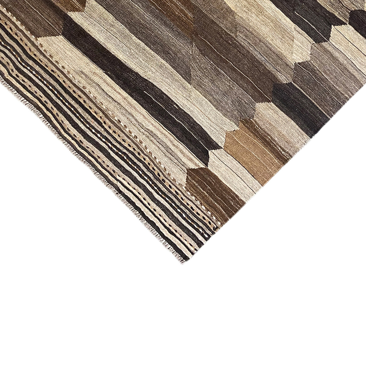 Corner of a kilim rug with a jagged border and fringe along the edge
