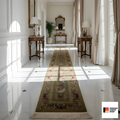 Silk runner with a green and beige background, floral borders, and fringes; in an elegant hallway