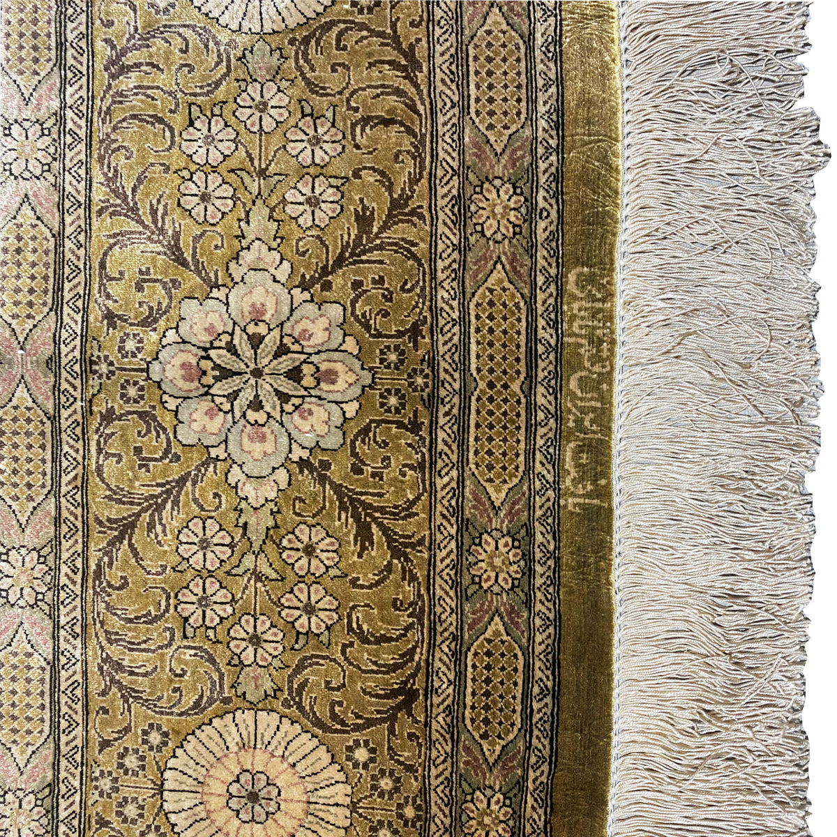 Carpet detail with a golden-brown pattern, floral ornaments, border stripes, and white fringes