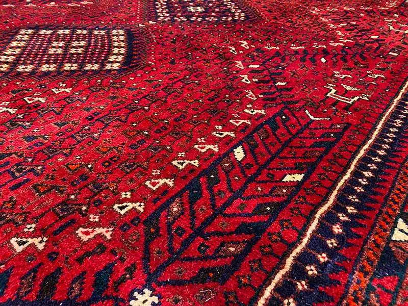 Close-up of a carpet: red geometric pattern with blue accents, border trim, and diamonds