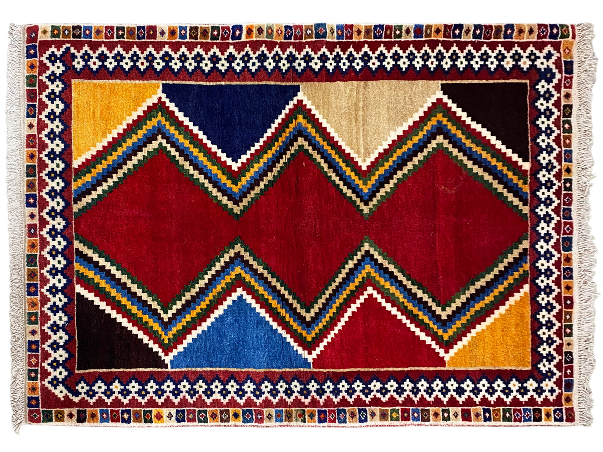 Rectangular Shiraz rug with zigzag and diamond patterns in red, blue, yellow, and beige, with fringes.