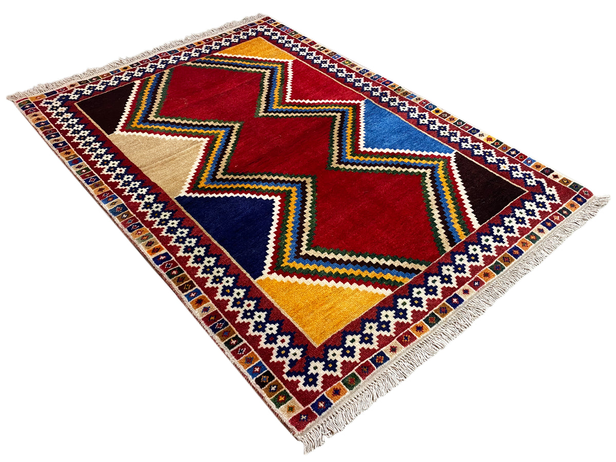 Square Shiraz rug with diamond and zigzag patterns in red, blue, yellow, and beige, with fringes.