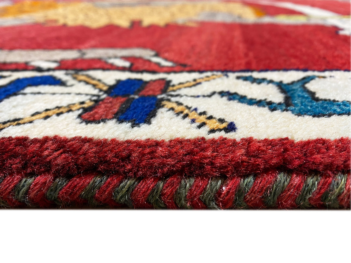 Carpet detail with a red pile surface, colorful patterns, and a fringed edge on the side
