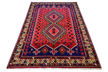 Rectangular rug with a red center, blue border, multicolored ornaments, and fringes