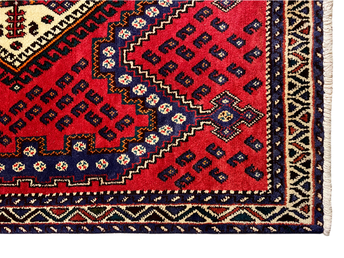 Corner detail of a red runner rug with a border, decorative stripe, and fringe