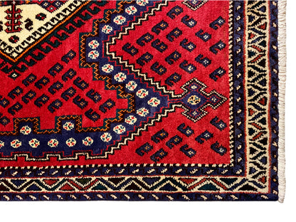 Corner detail of a red runner rug with a border, decorative stripe, and fringe