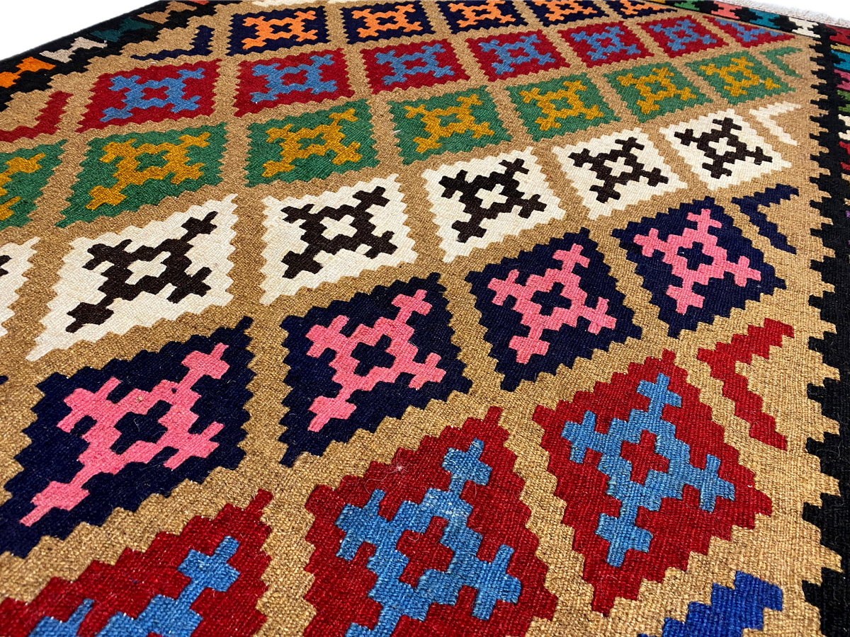 Kilim rug detail: geometric diamonds in beige, blue, red, and purple on a dark background.