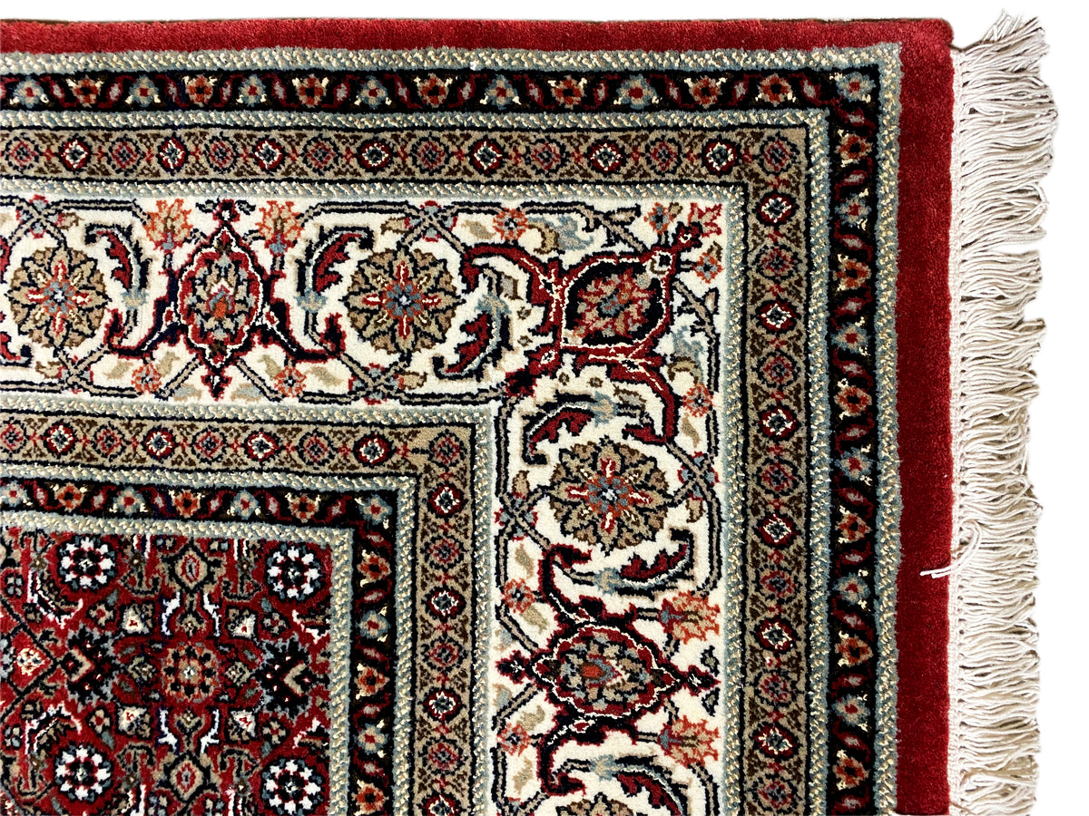 Corner of a Bidjar rug with fringes, a reddish-brown border, and a cream-and-black ornamental pattern