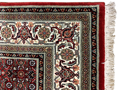 Corner of a Bidjar rug with fringes, a reddish-brown border, and a cream-and-black ornamental pattern