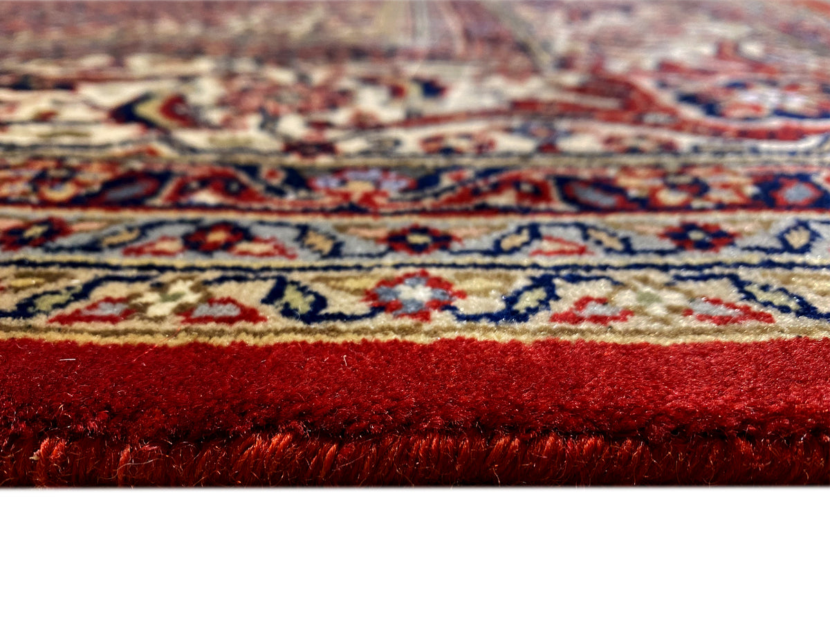 Close-up of a Bidjar rug: dense red pile with colorful patterned lines along the edge