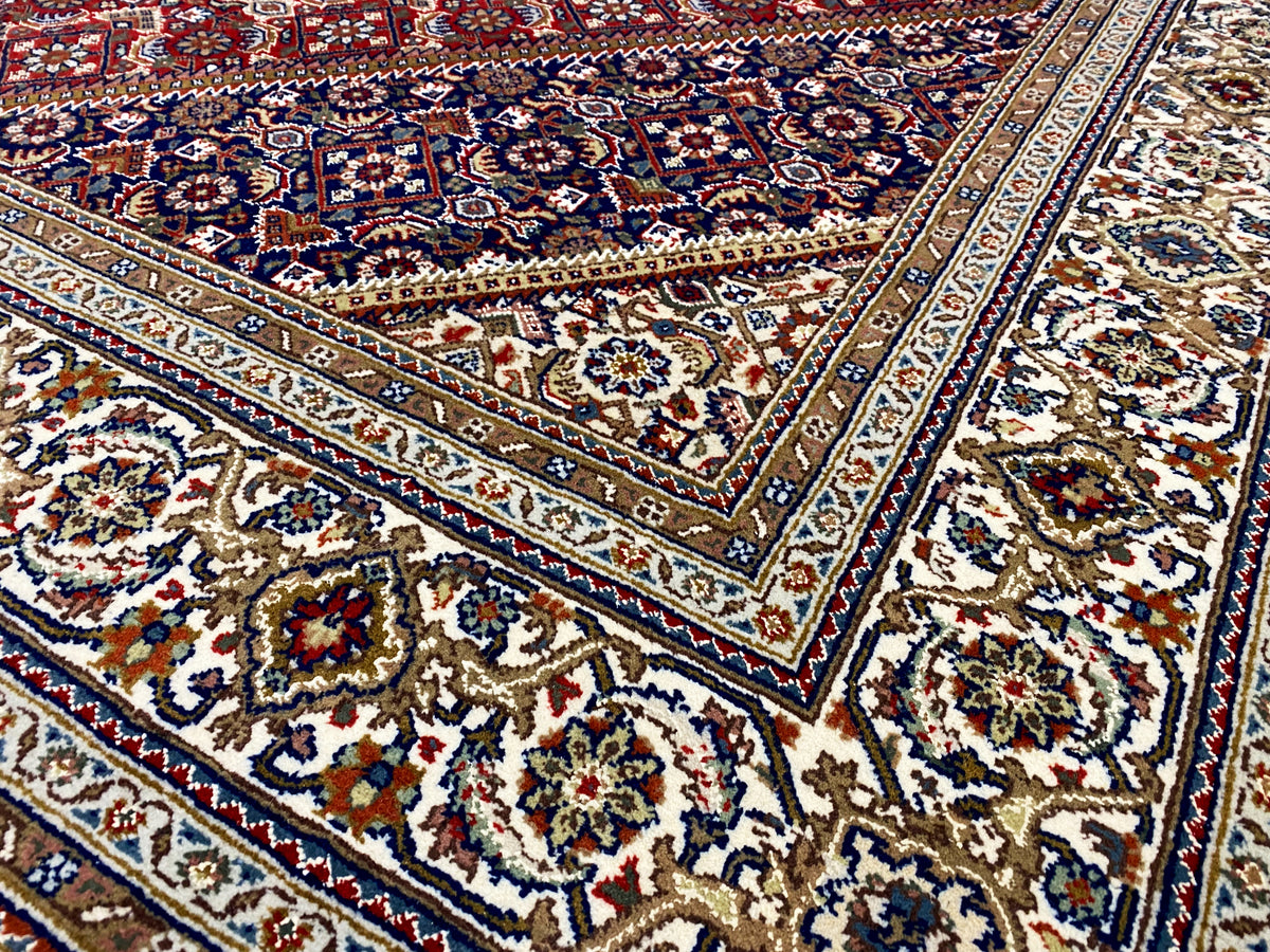 Close-up: carpet with a blue-and-white border, red panels, and intricate ornaments