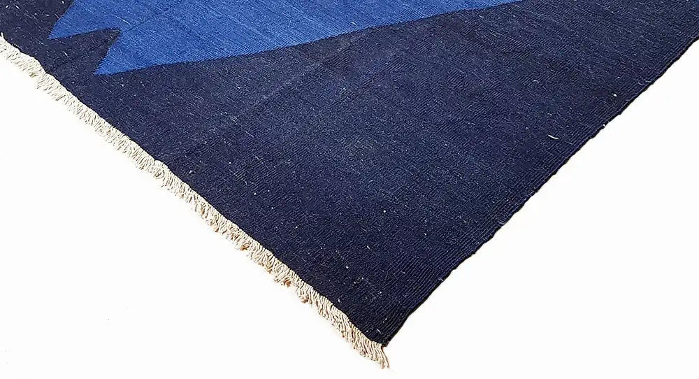 Corner of a blue rug with dark blue fabric and delicate fringe trim