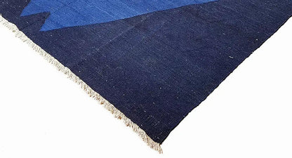 Corner of a blue rug with dark blue fabric and delicate fringe trim