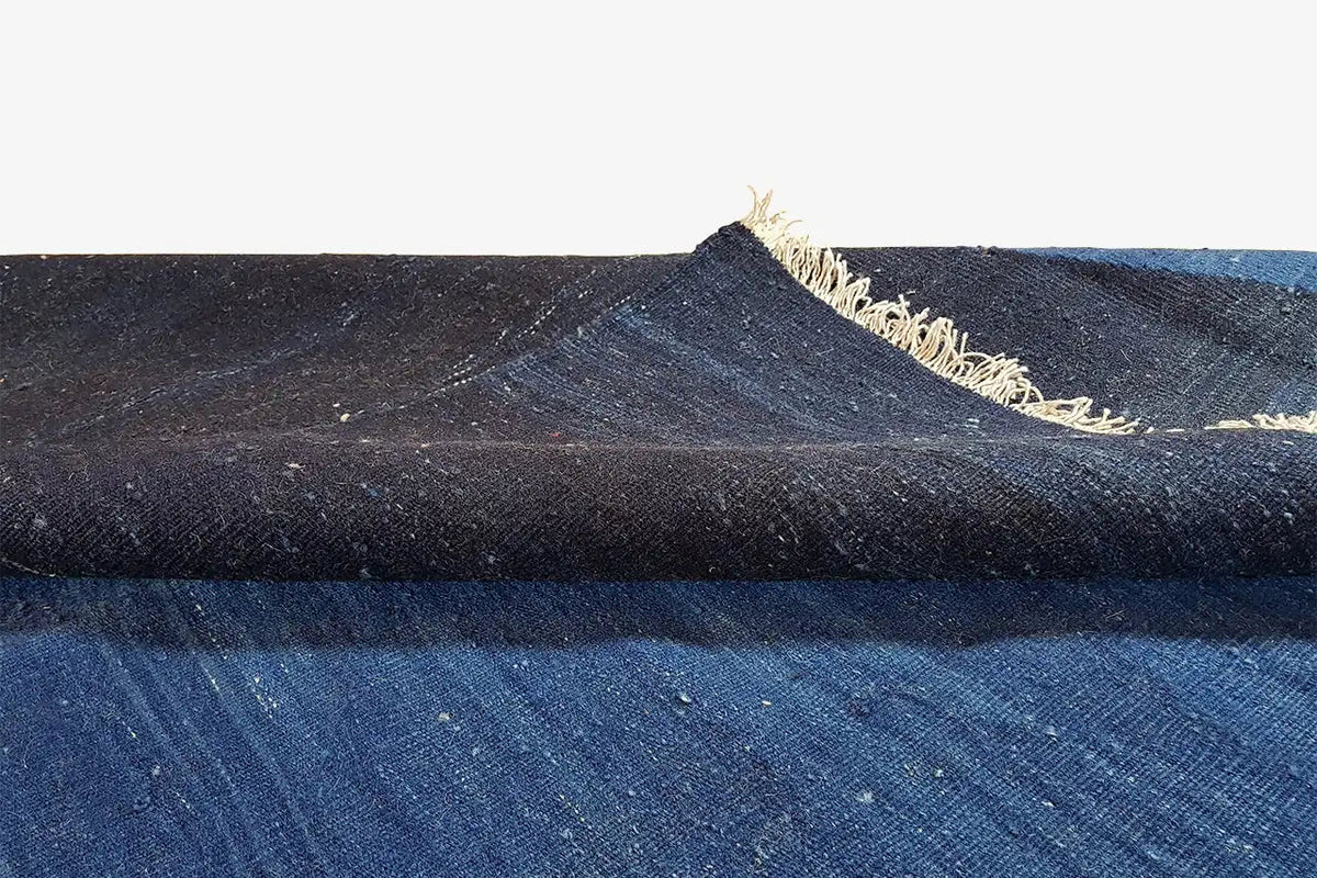 Close-up of rug edge: dark blue fabric with a beige fringed trim