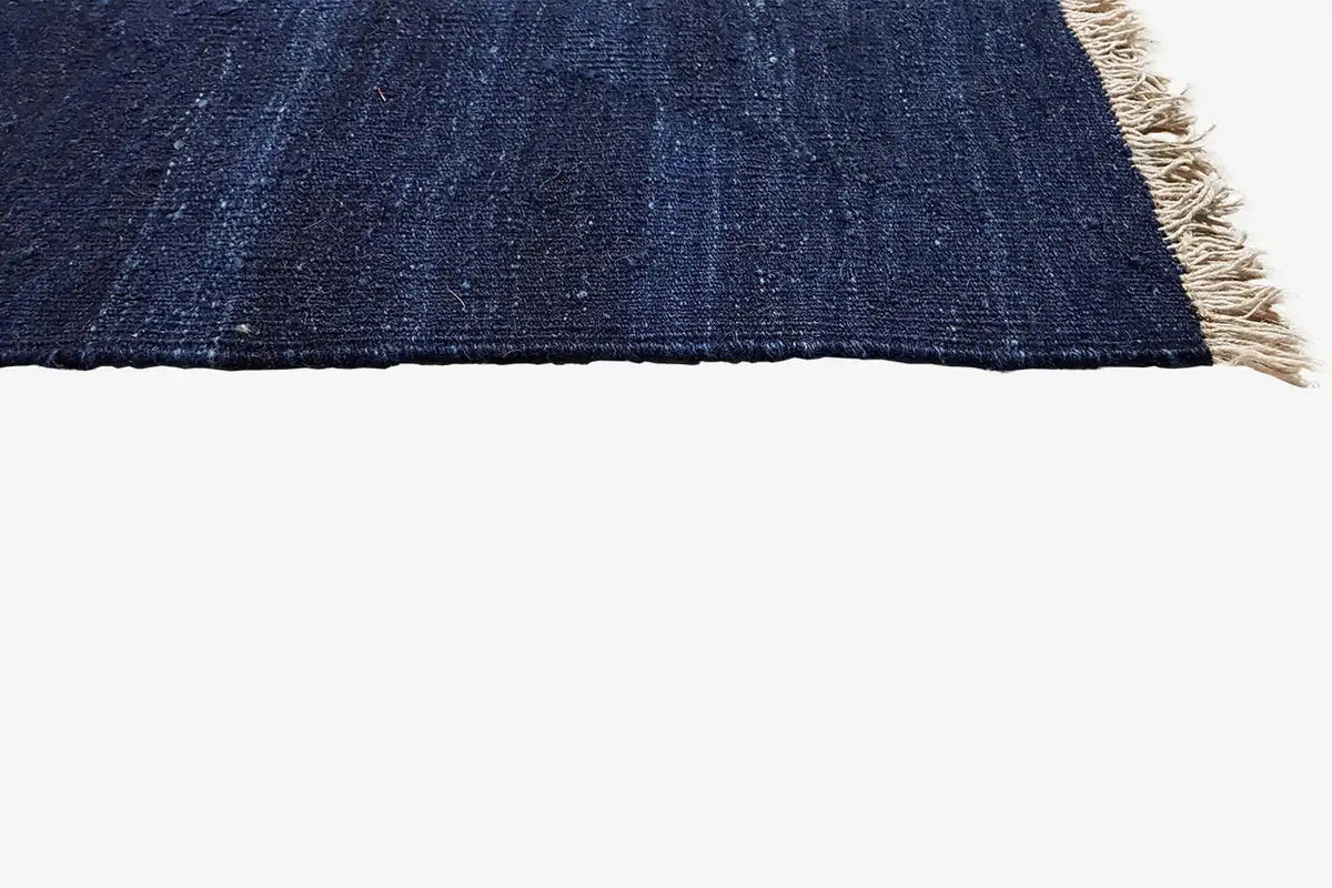 Carpet edge with beige fringes; dark blue fabric with a blue pattern visible at the cut edge