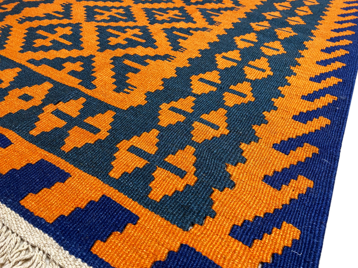 Kilim rug with an orange-yellow and dark blue woven pattern, close-up