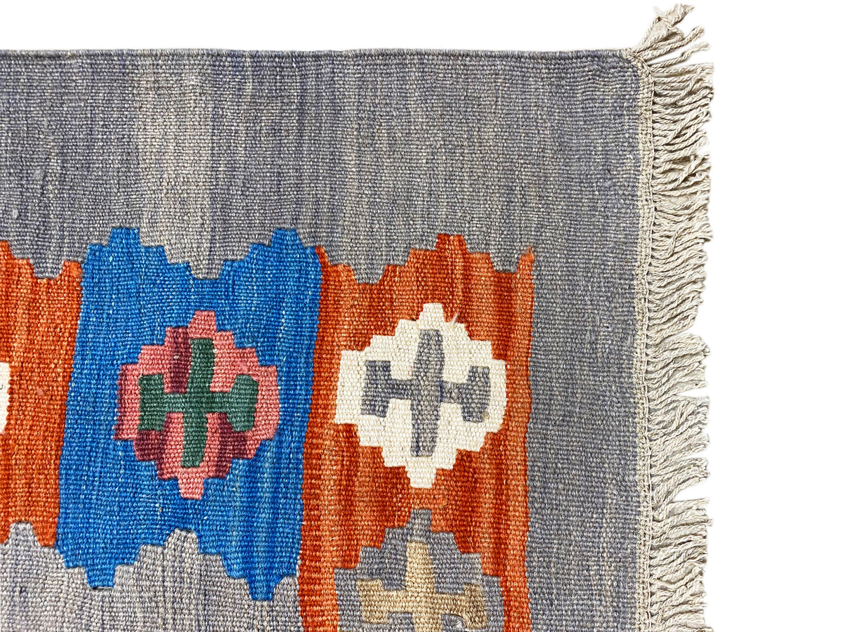 Gray mottled kilim rug with colorful diamond patterns and a frayed edge
