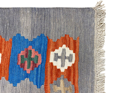 Gray mottled kilim rug with colorful diamond patterns and a frayed edge