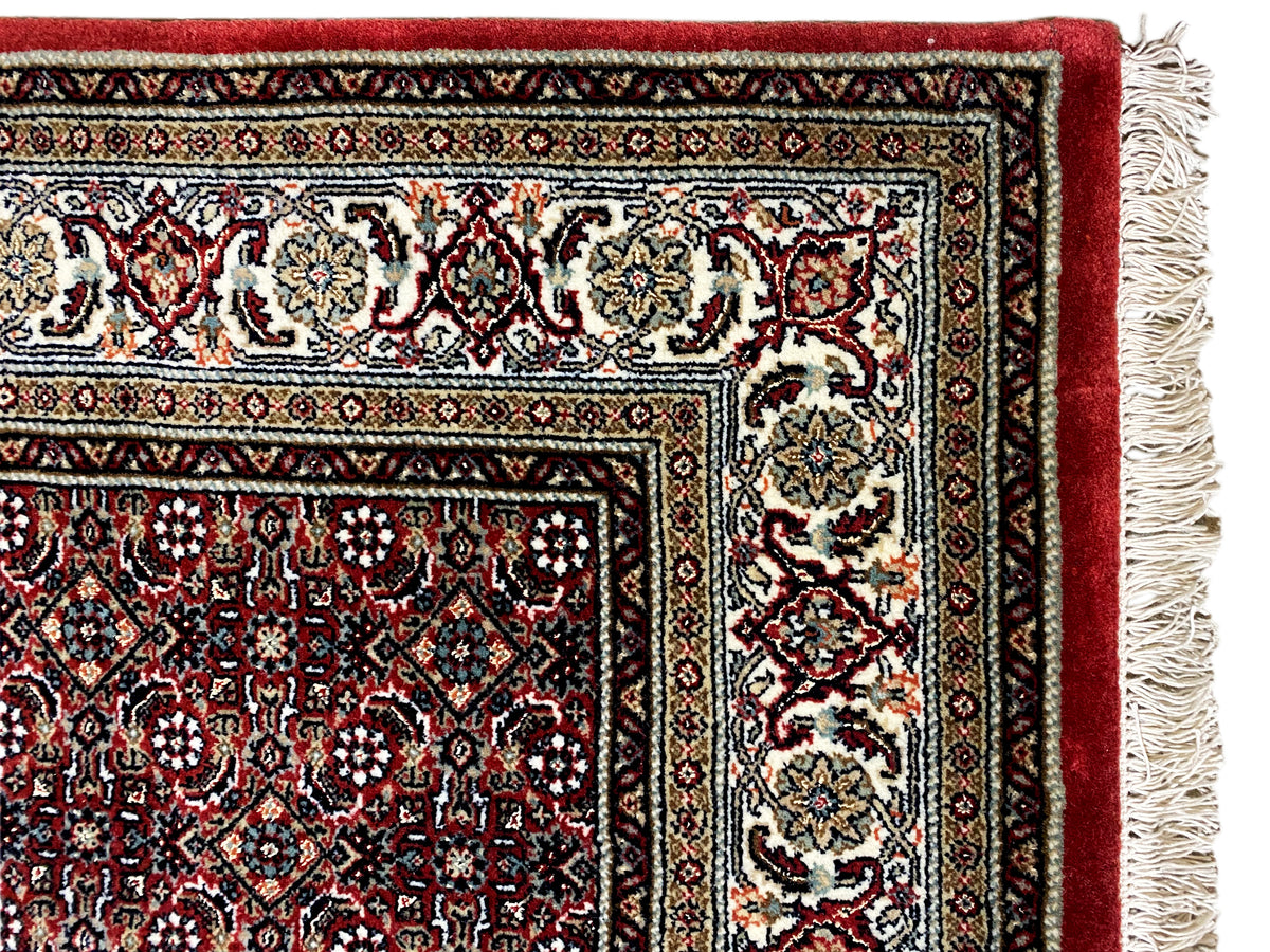Bidjar rug corner with fringes: cream-colored motifs on a dark red background
