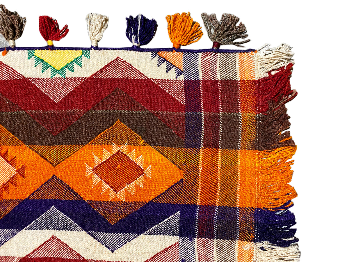 Jajim rug corner with tassels in orange, blue, white, and brown, dense checkered pattern