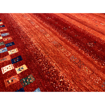 Close-up of a Gabbeh rug: reddish texture with a glitter effect and part of the multicolored border