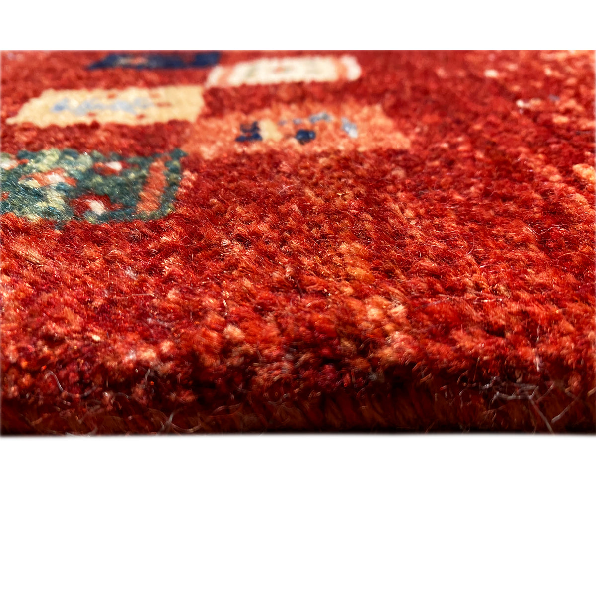 Close-up of a Gabbeh rug: dense red pile with multicolored pattern fragments
