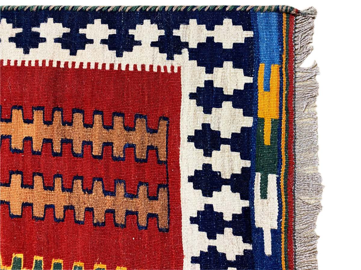 Kilim rug with a red and blue pattern, multicolored stripes along the edge, fringes