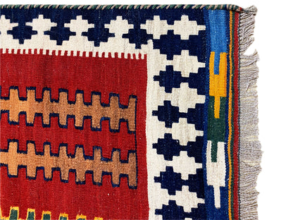 Kilim rug with a red and blue pattern, multicolored stripes along the edge, fringes