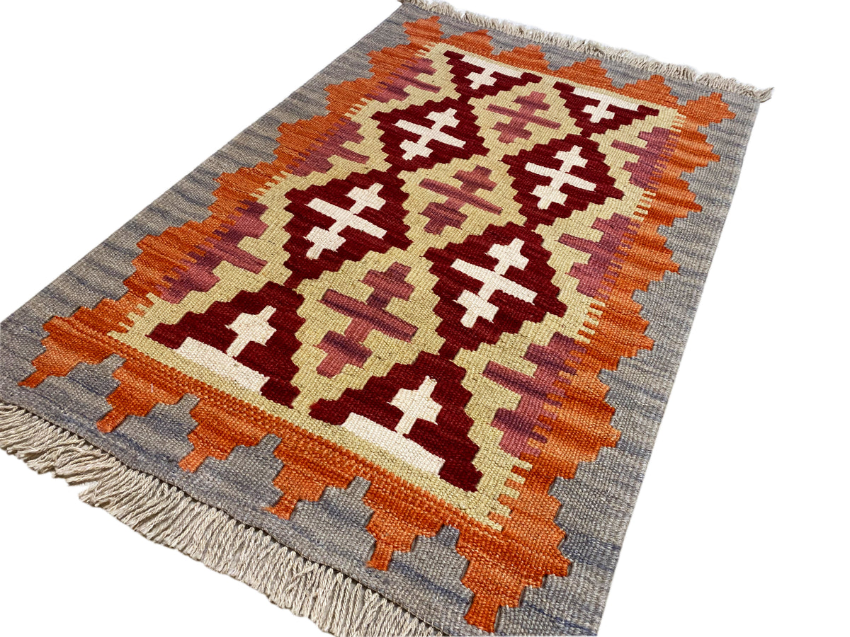 Angled kilim rug: graphic ornamental pattern in orange, cream and dark red on gray