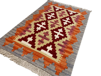 Angled kilim rug: graphic ornamental pattern in orange, cream and dark red on gray