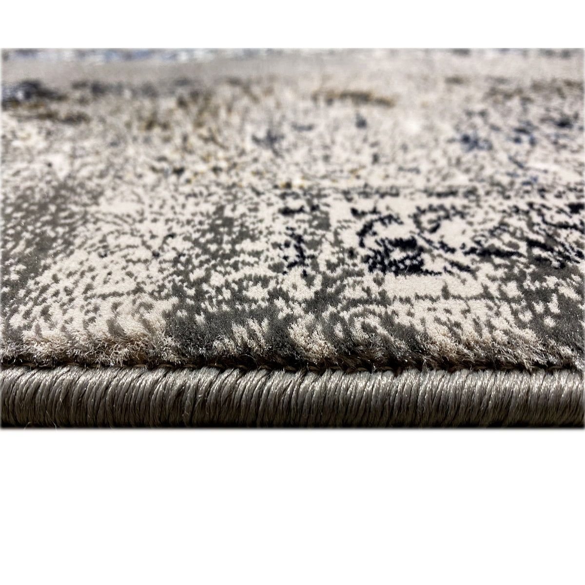 Carpet edge with fringe and dense pile; gray-brown surface with blue shading in the pattern