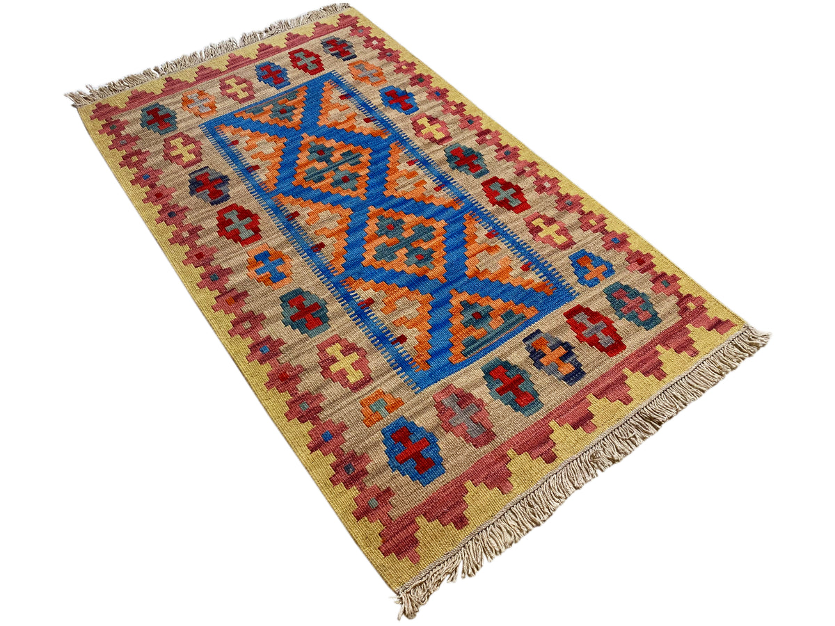 Beige kilim rug with a blue-orange central motif and colorful border ornaments, fringes