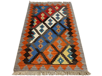 Kilim rug with geometric pattern, gray base, orange, blue and red accents, fringes