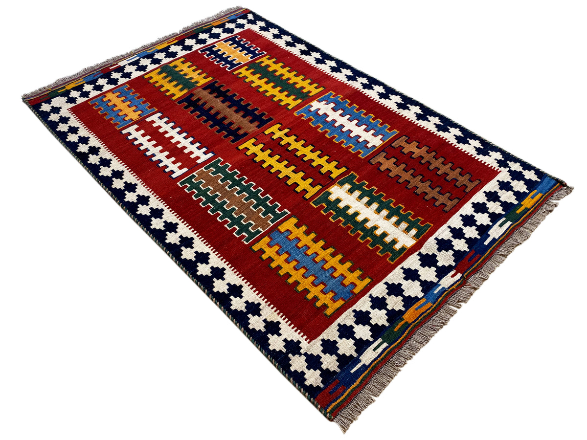 Red kilim rug with a blue border, geometric diamond design, and fringe