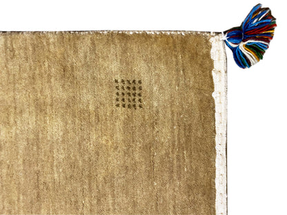 Light brown Gabbeh rug with a white border and blue tassel trim at the corner