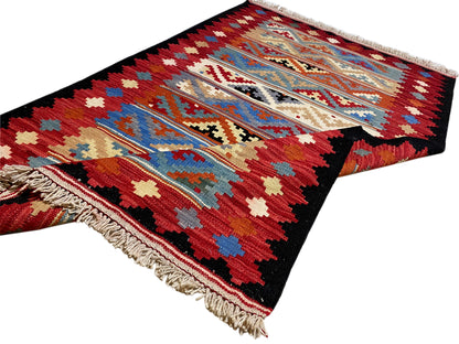 Kilim rug with a geometric pattern in red, blue, and beige, with fringes along the edge.